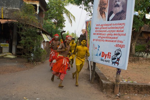 God and Communism: Kannur, Kerala, India: Theyyam performers returning after cock-sacrifice. The juxtaposition of traditional Hindu ritual and the communist banner in the background reflects the current political scenario in Kannur, Kerala. Even to the present day Kannur district is a strong hold of communist party in Kerala.