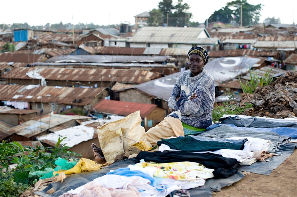 woman is selling clothes, surrounded by garbage. On backgrond Kibera village