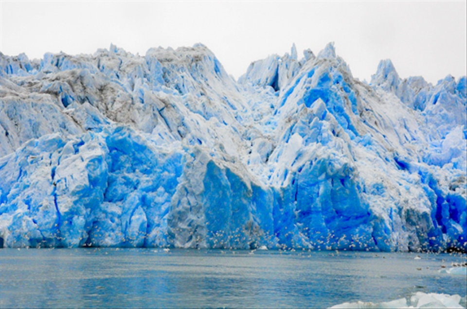 Seagulls and other birds -tiny looking- fly low in front of millions year old ic