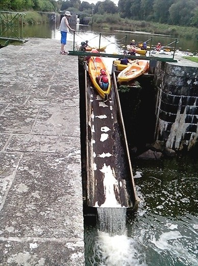 A group of children kayaking down the overflow ramp by the lock.