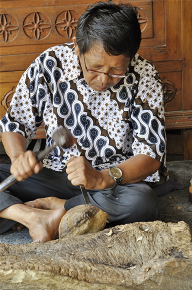 A Balinesian man carves wooden sculptures for tourists to buy. Tour leaders take groups to many destinations like this to watch the workers create wood carvings, jewelry or batik fabrics and make purchases. Incentives are given to the guides if tourist buy items.