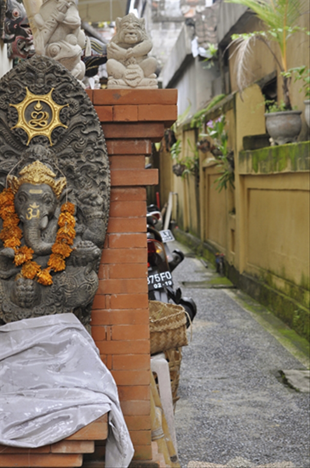 A shrine to a Balinesian god is on a wall near an alley with a motor bike in the background showing how the Western world and tourism has influenced the Balinesian culture.  Now it is a mix between modern ameneties like motor bikes and keeping with the traditional culture in Bali.