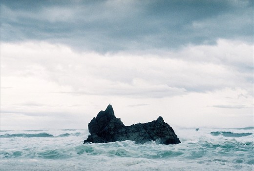 The lone black jagged rock pierced the swirling ocean and darkening skies