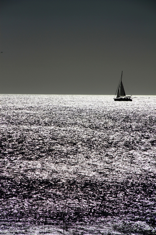Sailboat seems to be attached  to the sea. Almost like a drawing on the horizon.