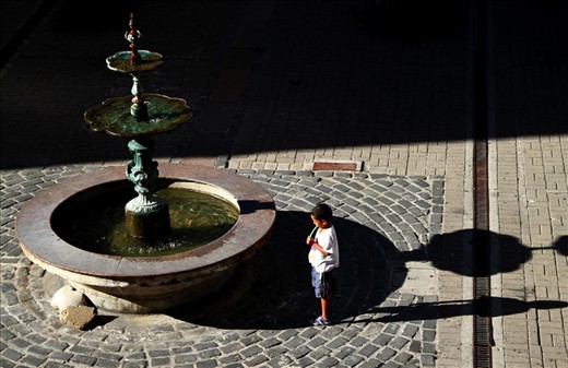 A young kid waits for someone at the downtown fountain.