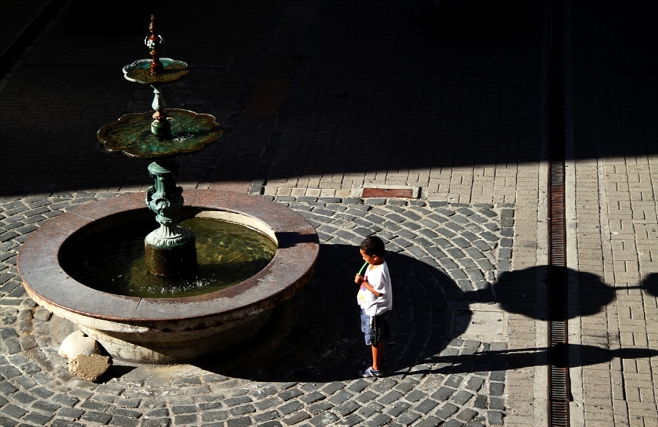A young kid waits for someone at the downtown fountain.