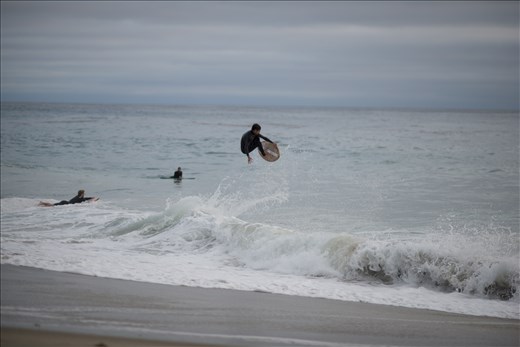 A skimboarder jumps up from a wave as friends watch
