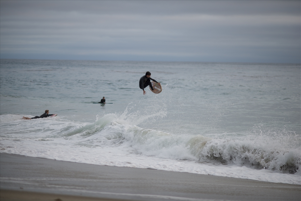 A skimboarder jumps up from a wave as friends watch