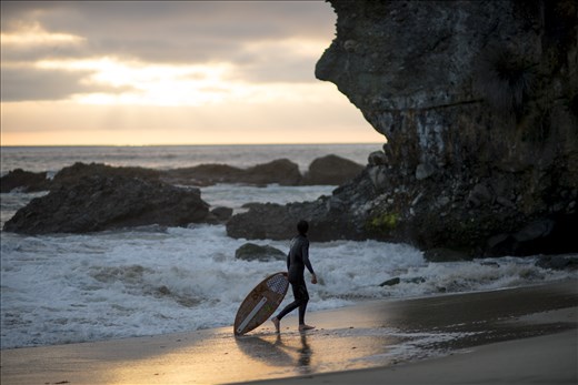 A skimboarder takes a break behind the rocks at Laguna Beach