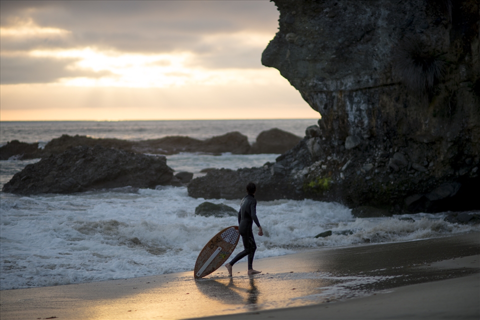 A skimboarder takes a break behind the rocks at Laguna Beach