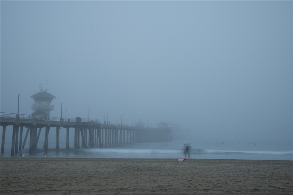 Foggy Laguna Beach Pier morning with surfers lining up for the perfect wave