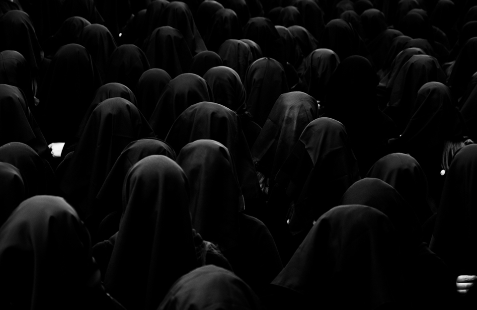 The women (around 250-300) cover their faces, as if to conceal their identity.