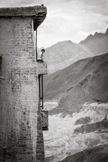 One of the most stunning aspects of Ladakh's many monasteries is their location. Nestled in the mountains and the foothills of the Himalayas, these monasteries offer some of the most breath taking views that one can only imagine or see in postcards. The calmness and serenity of these monasteries and the surrounding mountains is something that monks definitely derive from in order to maintain a sense of peace within them. Here we see a young monk sitting atop a balcony after completing his prayers.