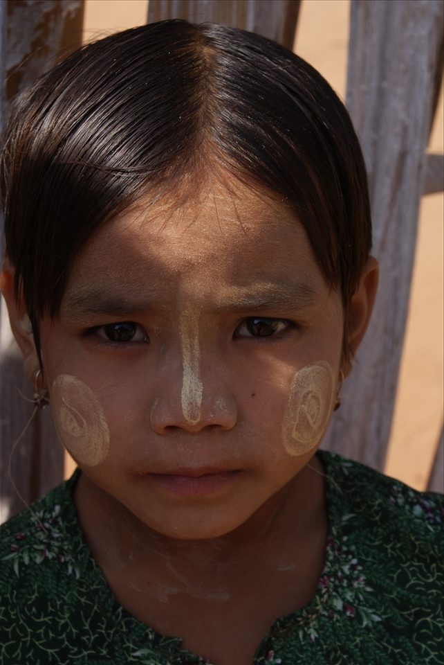 This young girl is wearing Thanaka paste. Thanaka is a yellowish white paste made from ground tree bark that has been used for at least two-thousand years in Myanmar. It has a fragrance similar to sandalwood and is said to have many protective properties. It is an effective sun-block and cools the skin. It is mildly astringent and is said to tighten pores and prevent acne. Traditionally Thanaka paste was worn in the months of July and August when planting rice seedlings in the paddy fields. Today it is applied year round to enhance beauty and for its fragrant aroma.