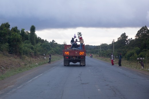 Four Kenyans celebrate hearing that Uhuru Kenyatta had just been ruled president of Kenya, on the back of a lorry they were travelling in. One of the men (far right) waves a branch at passing street merchants, who are also celebrating.