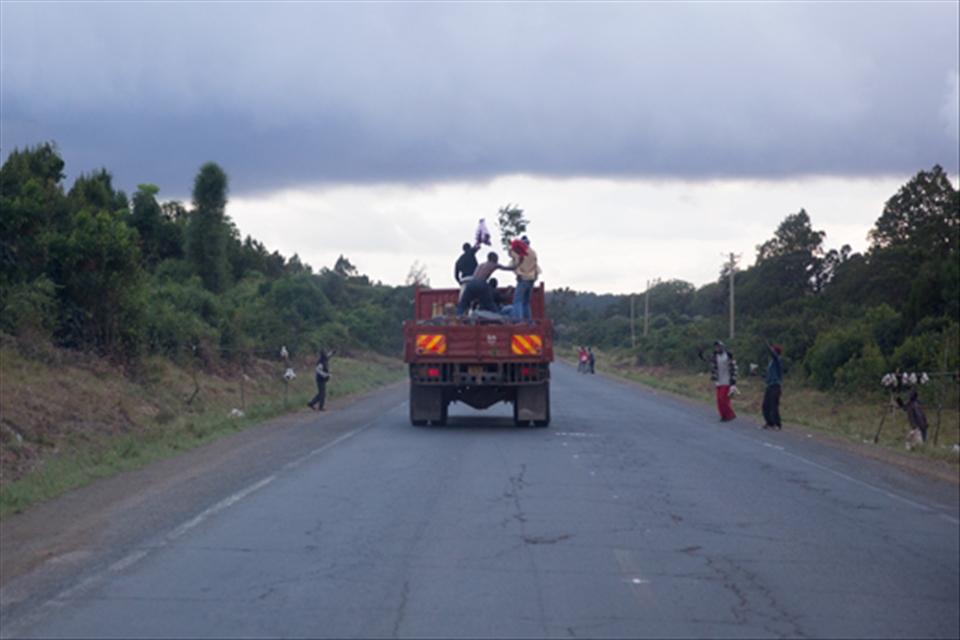Four Kenyans celebrate hearing that Uhuru Kenyatta had just been ruled president of Kenya, on the back of a lorry they were travelling in. One of the men (far right) waves a branch at passing street merchants, who are also celebrating.