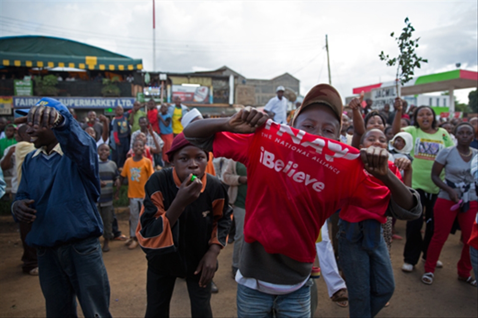 A young Kenyan boy shows his support for the National Alliance Party. It's leader, Uhuru Kenyatta, has just been elected president of Kenya. Other local Kenyans are also celebrating behind him.