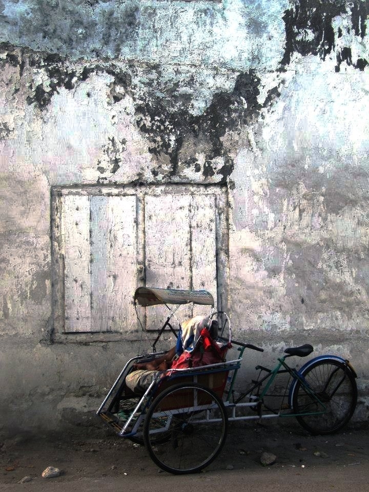 A becak driver is sleeping inside his becak. Becak is a traditional transportation tool in Indonesia. It's similar with pedicab. The drivers usually also sleep on their own becak in the night.