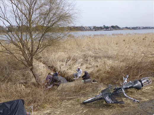I spotted these fishermen sitting together with their rods at this little stream exiting the lake. As Caucasian foreigners such as my brother and myself are still rather unusual in Japan, particularly in smaller neighbourhood areas such as these, one of them looked up at us, chuckled and pointed us out to his friends. One can only guess what his remark was, but it could have been along the lines of, “Eh? Gaigen!” (the Japanese word for foreigner).  
Their bicycles were all casually left on the side of the road, clearly showing their means of travel and the locality of their homes.