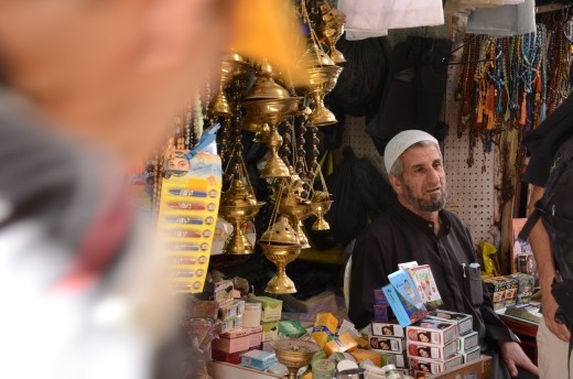 A shop owner in the old city of Jerusalem sits outside his shop selling traditional items and souvenirs trying to entice passing tourists. The narrow streets of the Arab market come alive with scents of fresh cooked falafel and perfumes.