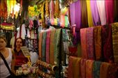 A shop owner hidden beneath swathes of hanging fabrics in bright colours in the Old City of Jerusalem. Beautiful fabrics in silk and cashmere hang outside to the attention of passing trade while 'traditional' costume hangs for the perfect tourist memento.: by sarahg, Views[551]