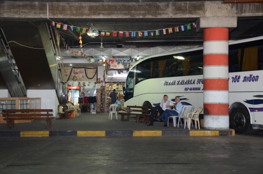 Two bus drivers sit waiting in the coach park for their tourists to return. The hanging flags from the buildings ceiling is representative of the different nationalities that visit every year whilst in the back ground a shop keeper sits awaiting custom. He sells tourist mementos of religious depictions along with postcards. Tourism is a vast source of income for the country.