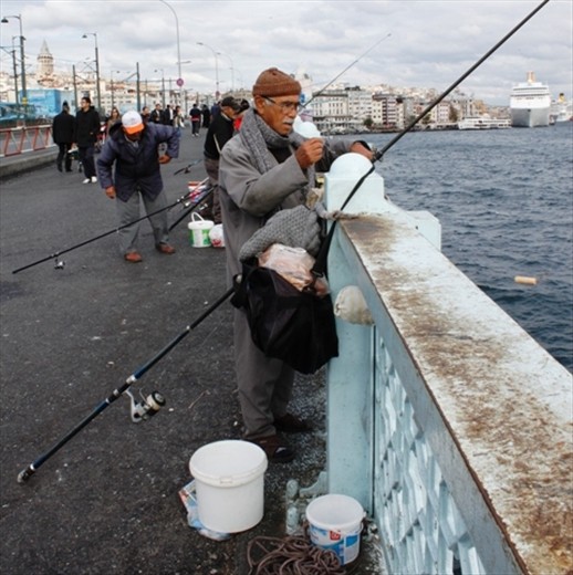 This fisherman has wrapped up warm for a long day holding his line. Accompanied by a deep bucket for his catch his aim is to fill it with migrating fish in the Bosphorus River.