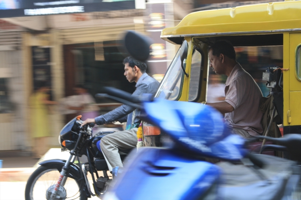 A motorbike and a rickshaw speeding through the busy streets of Panaji, with stern concentration, Goa, India.
