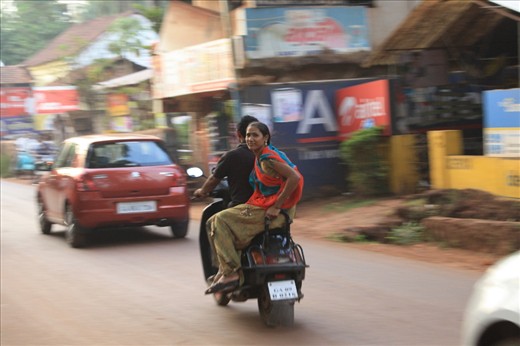 A women's pleasant and serene nature shining while she rides, side-straddle on the back of a motorbike, without protection, on India's notorious roads, Goa, India.