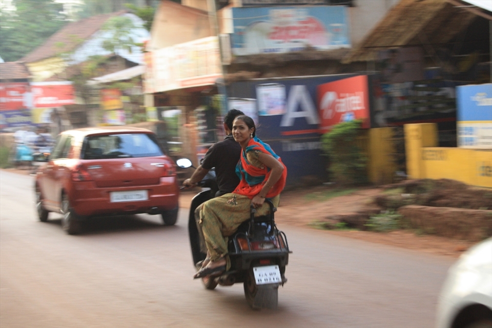 A women's pleasant and serene nature shining while she rides, side-straddle on the back of a motorbike, without protection, on India's notorious roads, Goa, India.