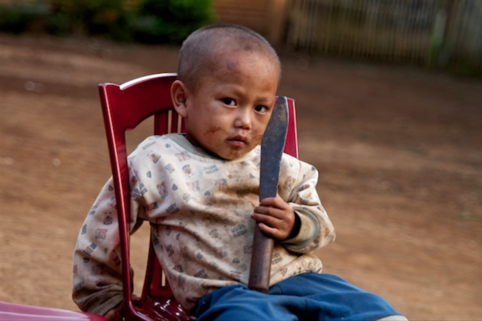 A young Hmong boy holds onto a machete used for chopping rice husk