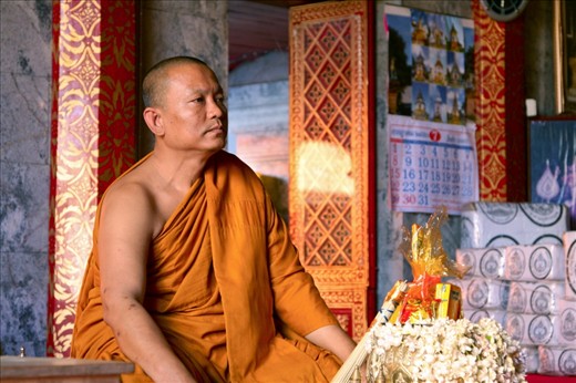 A Thai Buddhist monk sits unperturbed in his saffron coloured robe as cohorts of tourists admire the awe-inspiring architecture around Wat Phra Singh (the temple of the 