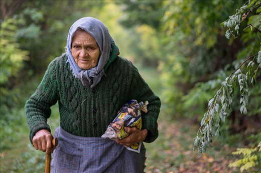 An old women is carrying food wrapped in a newspaper .