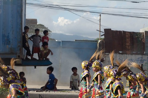 Children take cover from the blazing sun under the shadow of a large container truck as the parade begins.