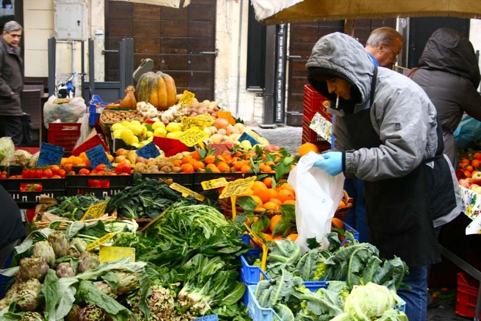 An open-air market, Campo di Fiori, is home to many tables of Italians selling their freshest fruit and vegetables. No matter rich or poor, native or tourist, everyone comes to this market to either buy food or watch common scenes of life unfold. A woman carefully selects only the best blood oranges for herself.