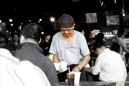 A seemingly 80+ year old man waiting a table at a local coffee shop at Vivo City, Singapore. The man and many other elderly folk like him in Singapore symbolize the undying spirit of the city
