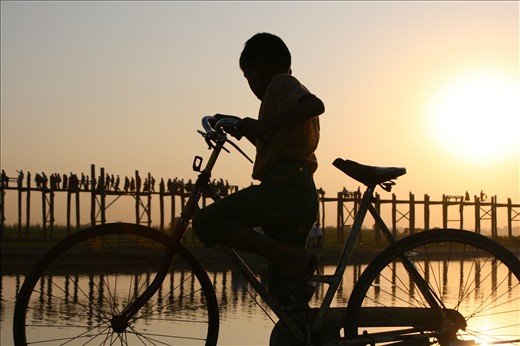 Boy is biking around U Bein bridge in Mandalay