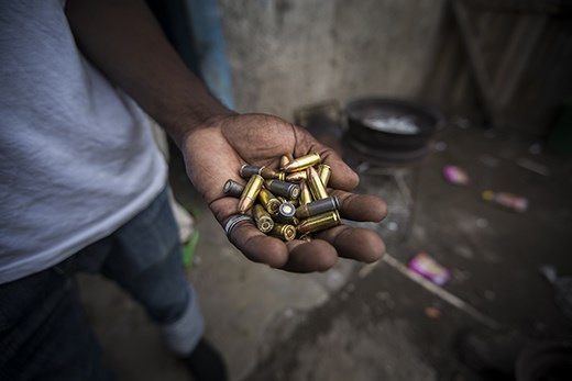 A gang member in Kingston, Jamaica holds a handful of bullets in his backyard.