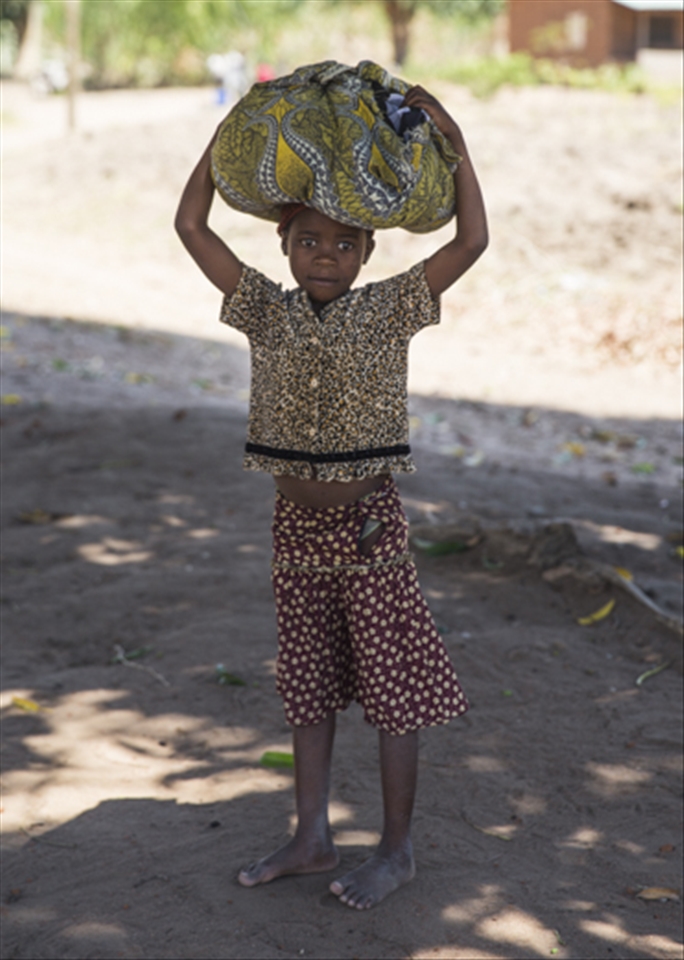 Passed on from ancient traditions, women including this young girl still carry loads on their heads where there is no less expensive, or more efficient, way of transporting things. Sometimes, women and girls carry up to 70% of their body weight on their heads. Men and boys are not seen doing this generally.