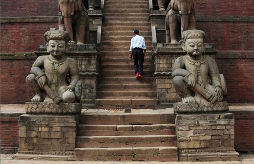 A solitary man ascends the stairs of a temple Patan Durbar Square, amidst crowds of tourists and merchants.  