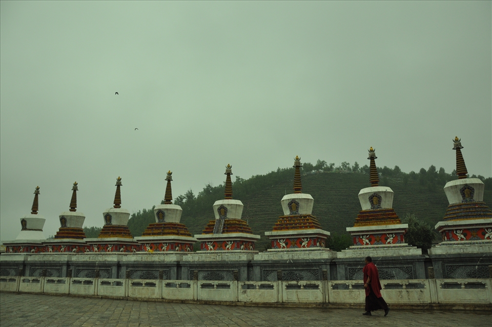 A monk walks by a monastery's mountain-side pillars in Qing Hai.