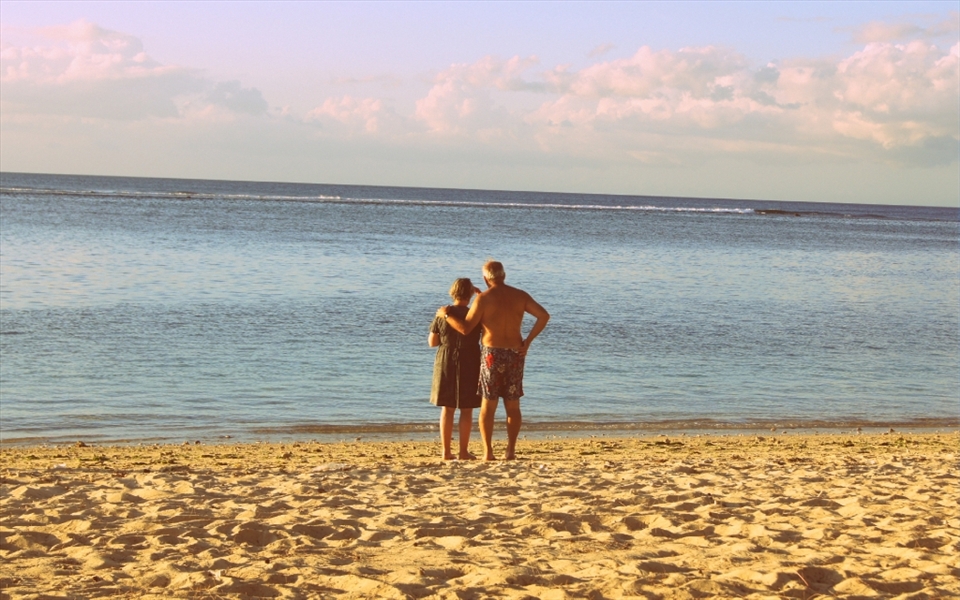 Elderly loving couple on beach at Flic en Flac, Mauritius, staring into the horizon, showing that the possibility of soulmates exist.