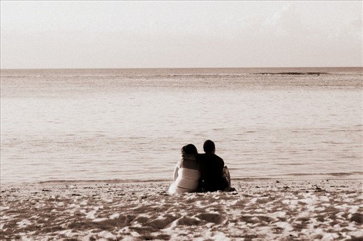 Young couple cuddling by the shore, settled in their spot to admire the setting sun.