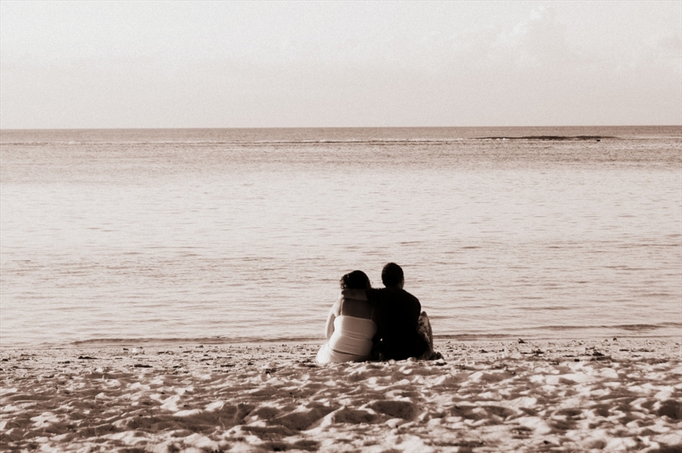 Young couple cuddling by the shore, settled in their spot to admire the setting sun.