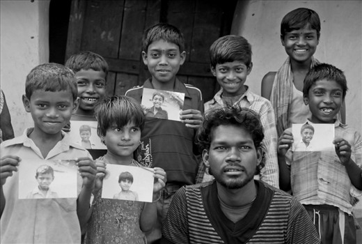 A bunch of kids along with an elder guy is all smiles, as they pose with their photographs. I had done a small Help-Portrait session with these kids on my visit to Huchukpara, whereby I gave them a print of their portraits. None of them ever had a printed photograph of themselves before and this simple gesture lit up their priceless smiles!  Notice Sujoy’s cheeky smile as he flashes his trademark unbuttoned pose in the photo.