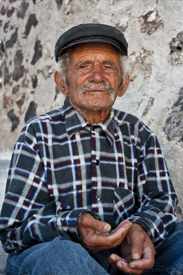 A beggar sits unnoticed amongst thousands of tourists as they flock to watch the sun set in Oia. 