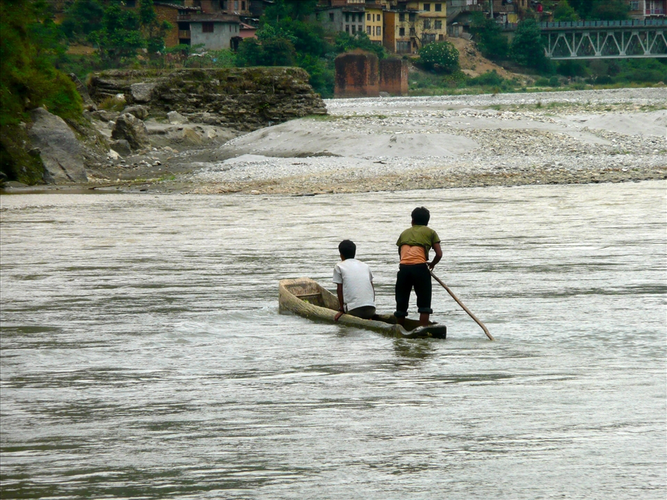 Two young boys travel down the river in their hand carved boat.