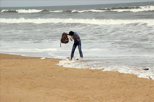 A boy juggling hard with his stuffs while protecting them from the sea waves.