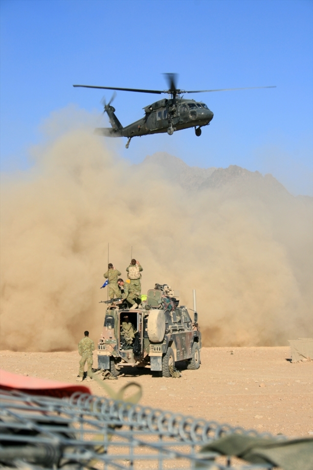 A US Blackhawk helicopter takes off, sending a cloud of dust towards excited soldiers capturing the event. For these men, this was their first taste of military deployment and of the dust of Oruzgan