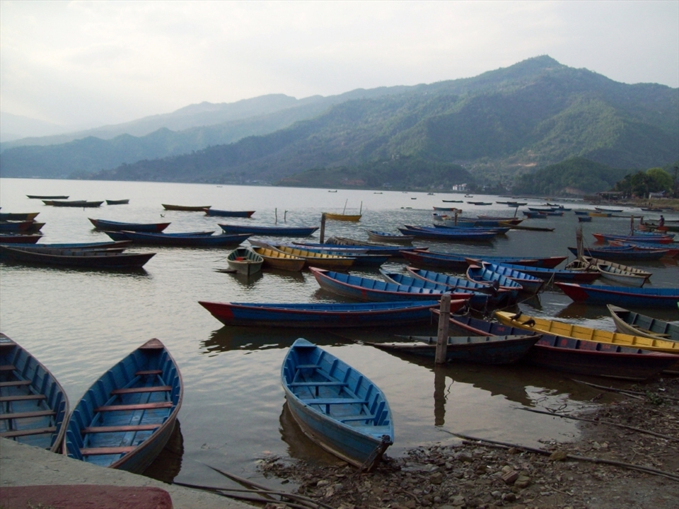 FISHING VILLAGE
This peaceful serene image captures a lull in activity of the contrasting colours and shadows of Nepalese fishing boats.  I love how all of the colours from the shoreline to the distant mountains complement the mood of the lake front.